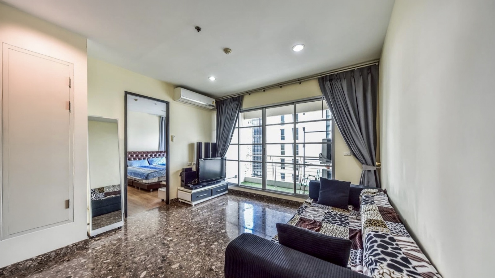 Living room with television, sofa, balcony windows, and the main bedroom doorway