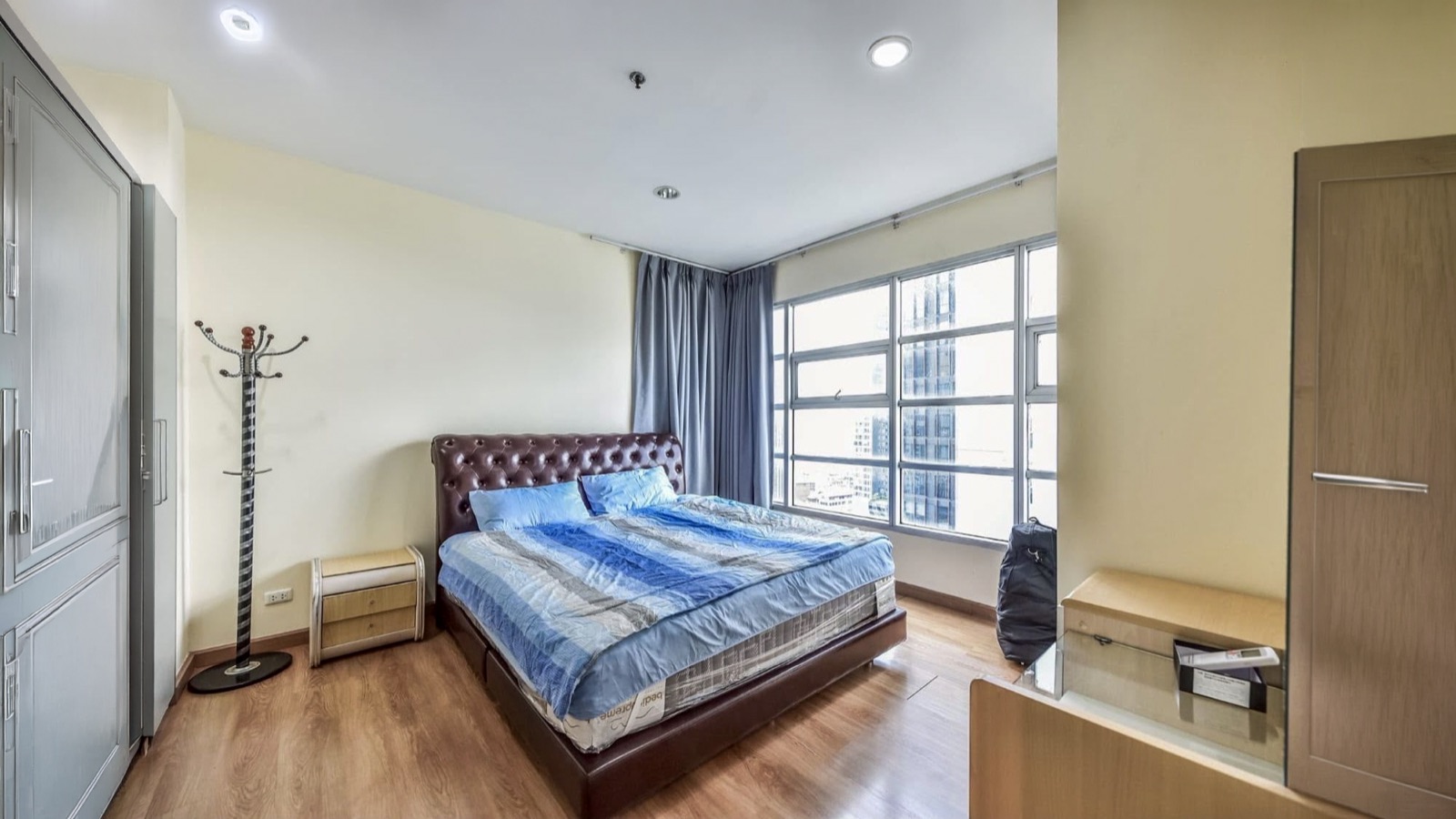 Main bedroom with a large corner window, bed, wardrobes, and vanity