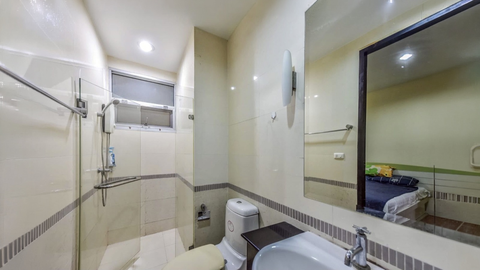 Second bathroom with glass shower, toilet, basin, and bedroom reflected in the mirror